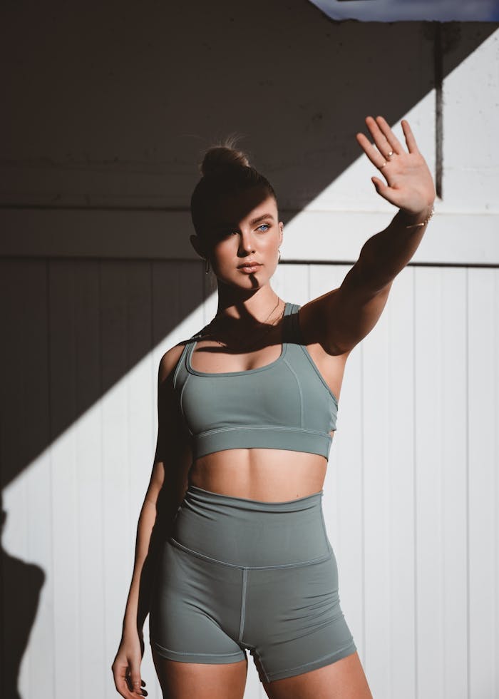 about-bg Portrait of a woman in gym wear outdoors, shielding face with hand under sunlight.